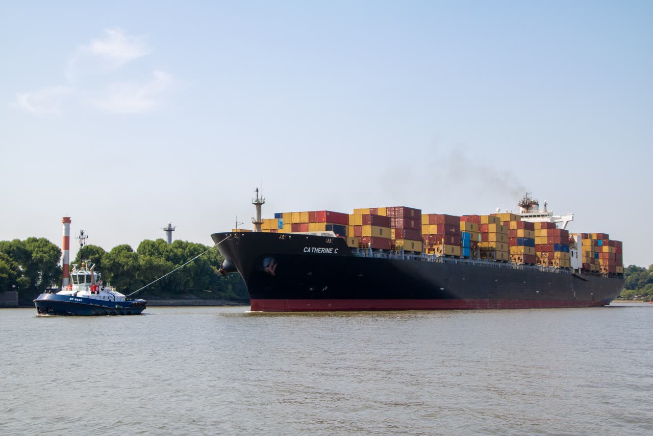 A loaded container ship on a river with a tug alongside